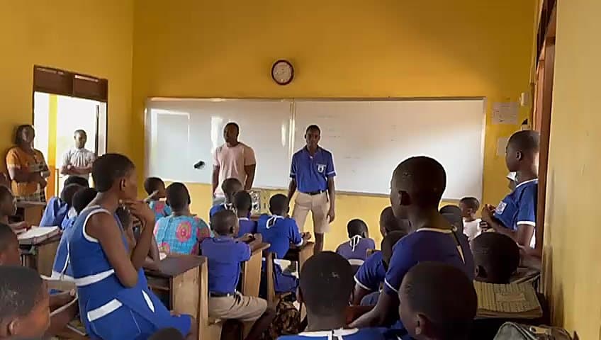 Foundation representatives addressing a full classroom of school children in blue uniforms during a visit