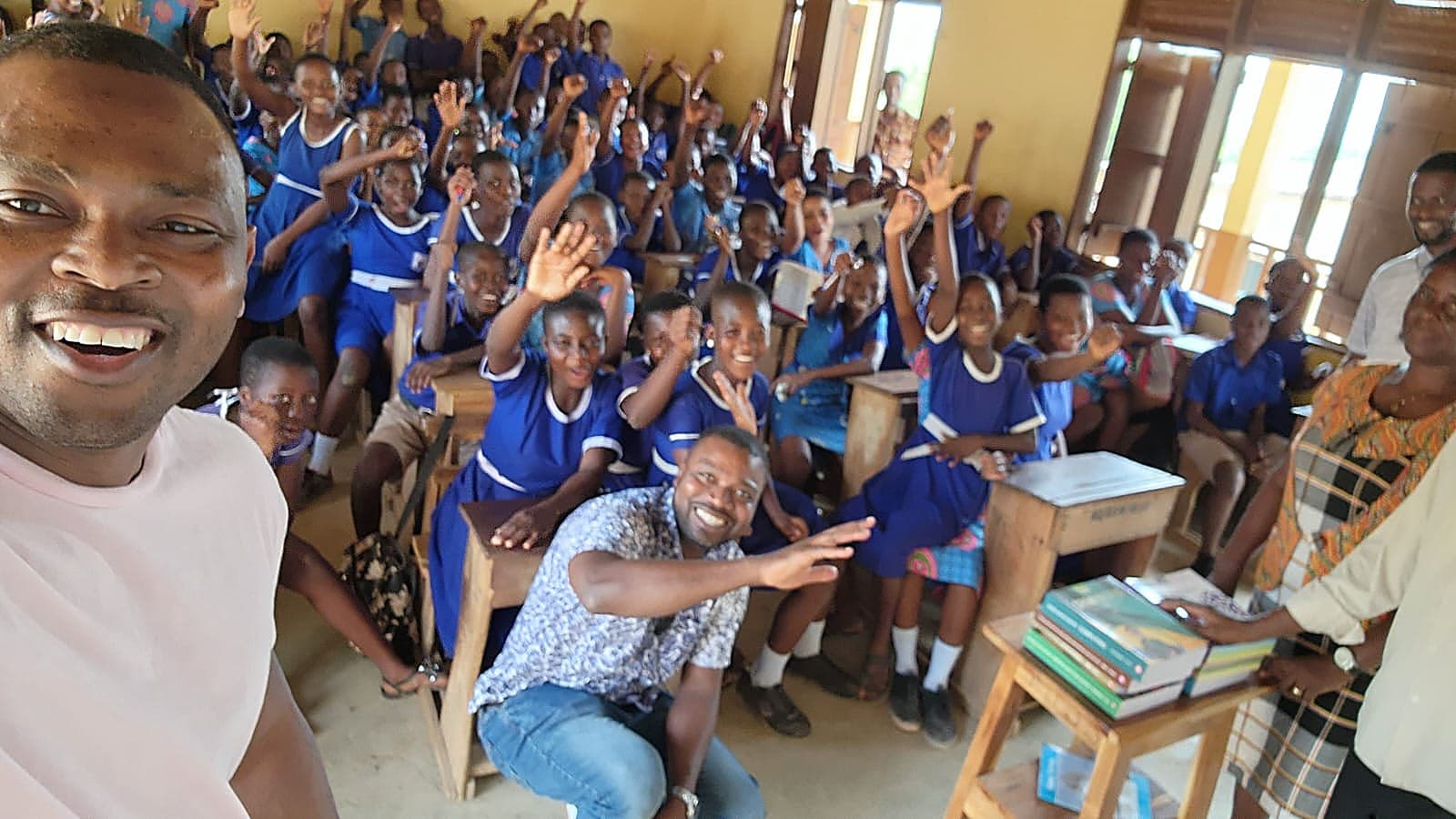 A packed classroom of school children in blue uniforms cheering with hands raised during a foundation visit